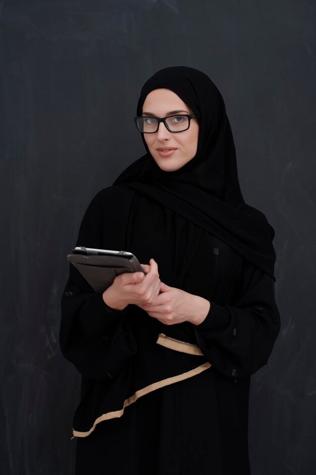 young-arab-businesswoman-traditional-clothes-abaya-glasses-holding-tablet-computer-front-black-chalkboard-representing-modern-islam-fashion-technology